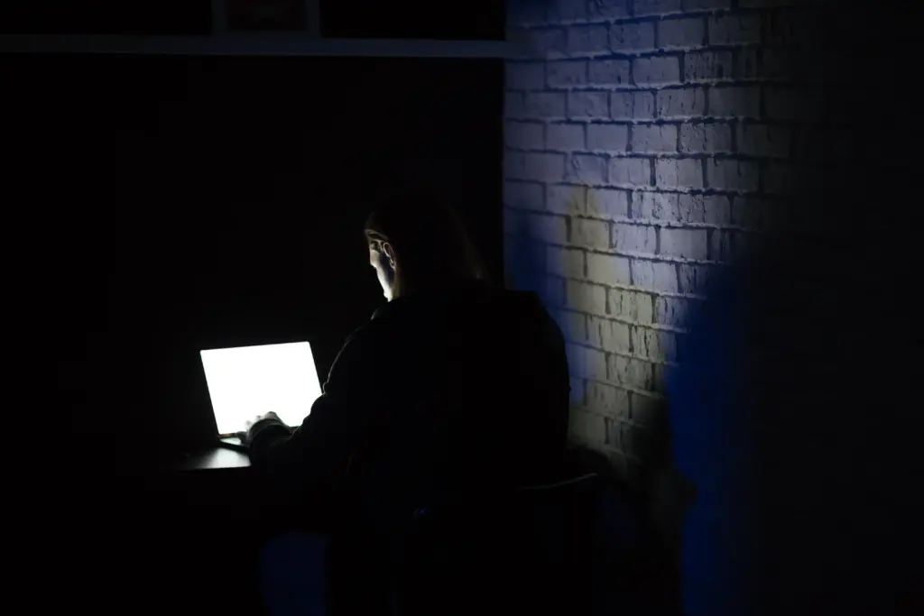 A poker player sitting in a dark room illuminated only by a laptop screen, representing the isolation of the online poker grind.