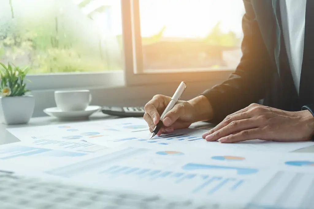 A person analyzing statistical charts and financial graphs with a pen, representing poker bankroll management and studying