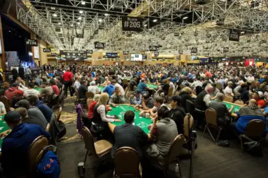 Large live poker tournament room filled with players at dozens of poker tables