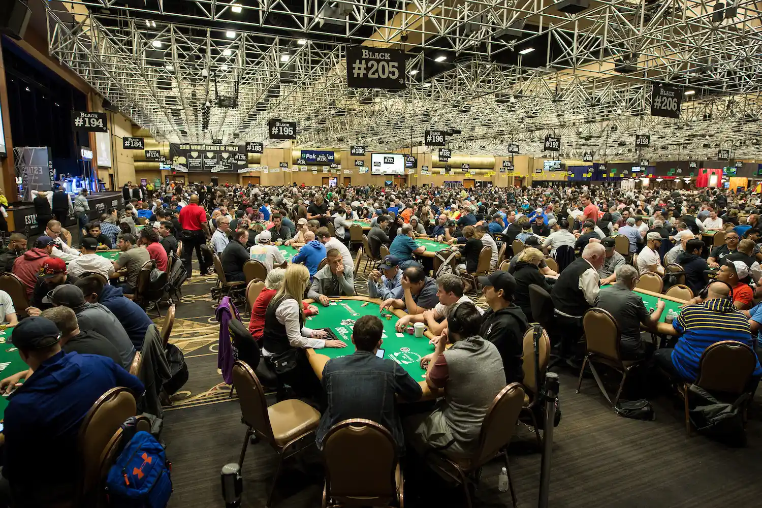 Large live poker tournament room filled with players at dozens of poker tables